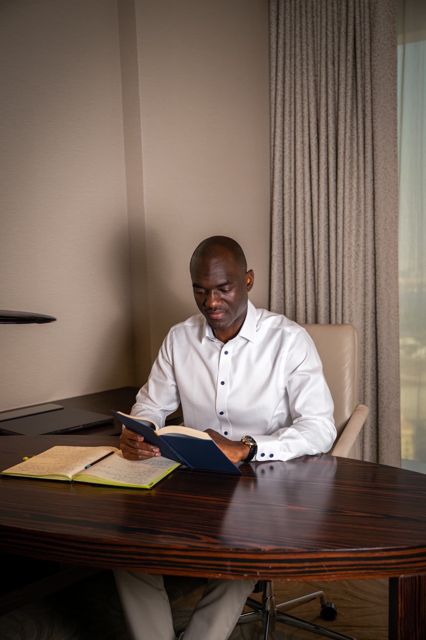 Tunde Cole reading at a desk with an open notebook